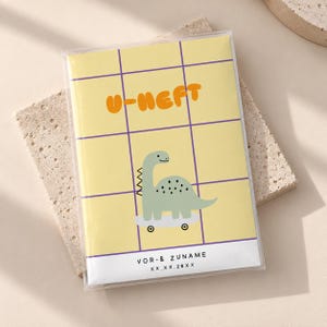 Könnte beinhalten: Ein rechteckiges Heft mit gelbem Einband und violettem Gittermuster. Der Text U-HEFT ist in Orange gedruckt. Ein hellgrüner Dinosaurier auf einem Skateboard ist mittig abgebildet. Unten stehen VOR- & ZUNAME sowie XX.XX.20XX.