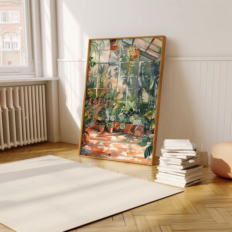 Puede incluir: Una pintura de acuarela enmarcada representa el interior soleado de un invernadero lleno de plantas en macetas. La obra de arte presenta una paleta de colores c&aacute;lidos con tonos de verde, marr&oacute;n y naranja. La pintura se apoya contra una pared blanca, junto a una pila de libros y una alfombra beige.