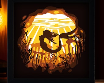 May include: A framed paper cut art piece featuring a mermaid silhouette swimming in an underwater scene. The artwork is layered with shades of brown and orange, with the text "DIGITAL FILE" in the top left corner.