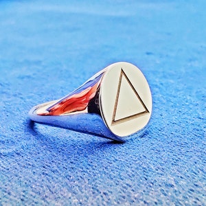 Peut inclure: Une bague en argent avec un visage rond orné d'un triangle gravé.