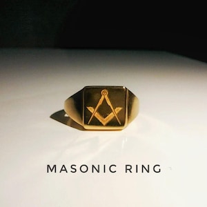 May include: A gold Masonic ring with a square face. The ring displays the Masonic symbol of a compass and square. The words "MASONIC RING" are printed below the ring.