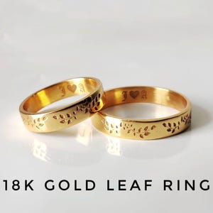 Peut inclure: Deux bagues en or avec des motifs de feuilles et des initiales gravées et un symbole de cœur. Les bagues sont en or 18 carats. Les bagues sont sur une surface blanche. Le texte "18K GOLD LEAF RING" est en dessous.