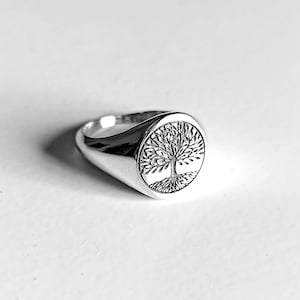 Peut inclure: Une bague chevalière en argent avec un motif détaillé d'arbre de vie. La bague a une finition polie et une face ovale arrondie avec les branches et les racines de l'arbre finement sculptées.