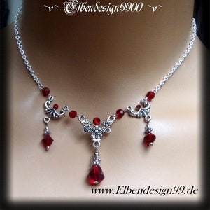 May include: A silver necklace with a red crystal pendant and two dangling red crystals. The necklace features ornate silver details and a chain with red crystal beads.