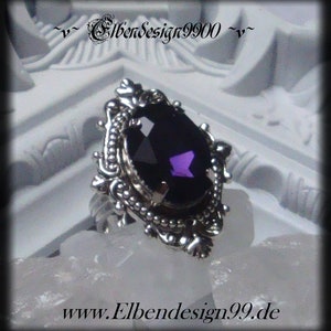 Op de afbeelding: Een zilveren ring met een sierlijke filigraan zetting. De ring heeft een grote, facetgeslepen, donkerpaarse edelsteen. De ring staat tegen een witte achtergrond. De website-adres "www.Elbendesign99.de" is zichtbaar.