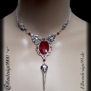 Può includere: Collana color argento con un grande ciondolo ovale di pietra rossa. Il ciondolo è impreziosito da un ciondolo a forma di teschio di uccello e dettagli di rose. La collana è esposta su un manichino. Il testo sull'immagine recita "Elbendesign99.de".