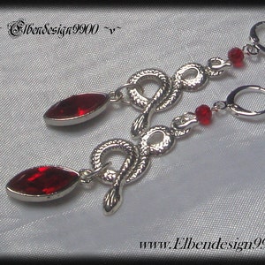 May include: Silver snake earrings with red crystal accents. The earrings feature a snake design with a red crystal at the bottom and a smaller red crystal bead on the snake's tail.