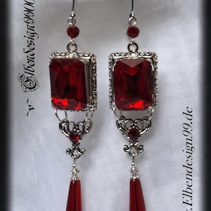 Könnte beinhalten: Ein Paar silberfarbene Ohrhänger mit großen, rechteckigen, rubinroten Edelsteinen. Die Ohrringe haben aufwendige Filigranarbeiten und tropfenförmige rote Anhänger. Der Text "Elbendesign9900" und "www.Elbendesign99.de" sind sichtbar.