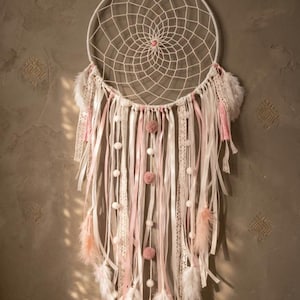 Handmade pink and white dreamcatcher with feathers and pom-pom for boho bedroom decor