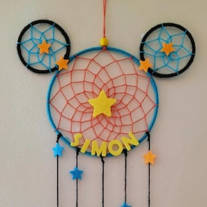 Peut inclure: Un attrape-rêves bleu et orange en forme de Mickey Mouse, avec le nom "SIMON" en lettres de feutre et des étoiles jaunes suspendues en bas.