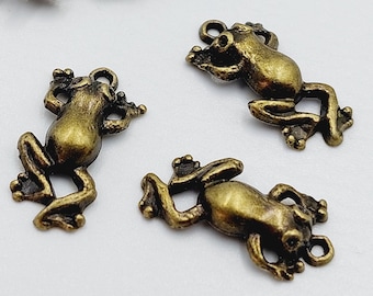 Può includere: Un set di sette ciondoli a forma di rana in oro antico. I ciondoli sono dettagliati e hanno un aspetto vintage.