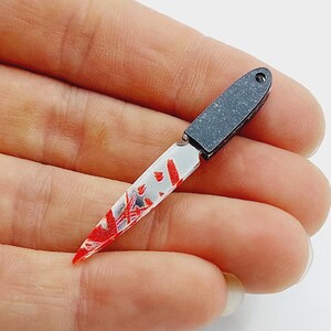 May include: A small, black-handled knife with a white blade and red blood splatter design.