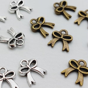 May include: A collection of silver and bronze bow charms. The charms are in the shape of a bow with a loop at the top for attaching to a necklace, bracelet, or other jewelry.