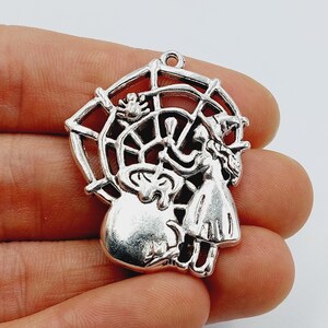 May include: Silver charm featuring a witch holding a broom and flying through a spiderweb. The charm is detailed and has a vintage look.