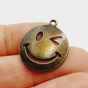 Può includere: Un ciondolo in metallo dorato a forma di faccina sorridente che fa l'occhiolino.