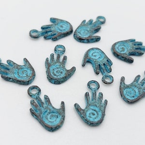 Peut inclure: Dix breloques en métal bleu turquoise en forme de main avec un motif en spirale. Chaque breloque a un anneau de saut pour l'attacher à des bijoux ou d'autres objets artisanaux.