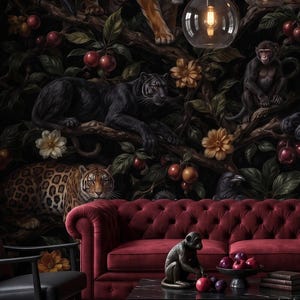 Pode incluir: Um sofá de veludo capitonê vermelho profundo fica em frente a um mural de parede escuro com tigres, leopardos, panteras negras e macacos entre folhagens e frutas vermelhas. Uma mesa de centro preta contém uma estatueta de macaco e frutas.