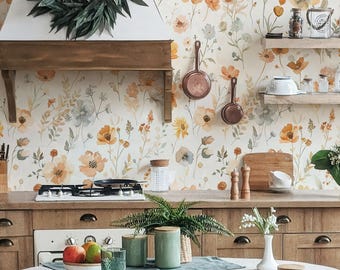 Puede incluir: Un interior de cocina con papel tapiz floral en tonos naranja y amarillo, gabinetes de madera y una mesa de comedor redonda con un mantel gris claro. Cuatro sillas de madera oscura rodean la mesa, que tiene botes verdes encima.