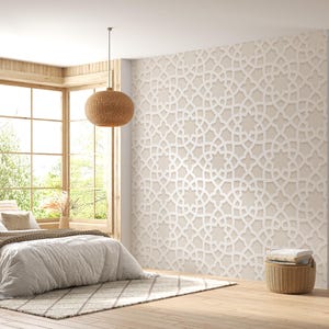 Op de afbeelding: Een slaapkamer met een neutraal kleurenpalet, met een groot bed met wit beddengoed en een bruine deken. Een patroonkleed en een decoratieve muur met een geometrisch ontwerp voegen textuur toe. Een geweven hanglamp hangt boven het bed en een groot raam biedt uitzicht op de buitenwereld.
