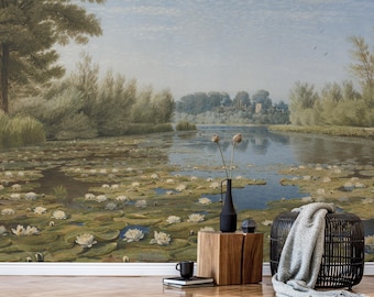 May include: A wall mural featuring a landscape painting of a pond filled with white water lilies, surrounded by trees and a distant building. In the foreground, a black vase with dried stems sits on a wooden block next to a black woven stool.