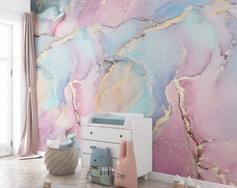 Peut inclure: Une peinture murale présentant un motif aquarelle abstrait dans des tons de rose, bleu et sarcelle avec des veines dorées. La peinture recouvre tout le mur derrière une table à langer blanche à trois tiroirs, un panier et deux coussins.