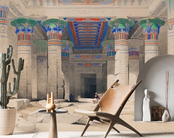 Puede incluir: Un mural de pared que representa el interior de un antiguo templo egipcio con grandes columnas de estilo papiro en azul, verde y rojo. La escena muestra ruinas de piedra, una puerta central y dos figuras pequeñas. Un sillón de cuero beige.