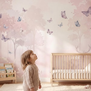 Puede incluir: Una habitación infantil con un mural rosa y morado de mariposas y un bosque. Una cuna de madera, una estantería y un niño mirando hacia arriba. Un oso de peluche y otros juguetes están en el suelo.