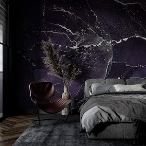 May include: A dark bedroom with a bed with gray linens and a dark headboard. A brown leather chair sits in the corner of the room. The wall behind the bed is painted a dark purple with white marble-like patterns.