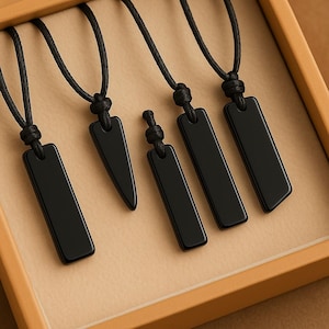 May include: Five black necklaces with different pendant shapes, including a triangle and rectangular shapes. The necklaces are displayed in a brown box.
