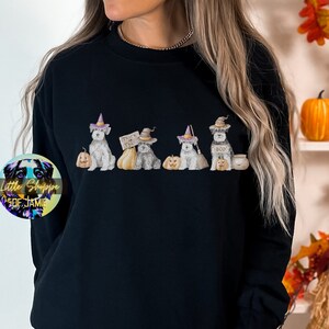 Puede incluir: Sudadera negra con un gráfico de cinco schnauzers en miniatura vestidos con disfraces de Halloween. Los schnauzers sostienen calabazas, un caldero y un cartel que dice "Trick or Treat".