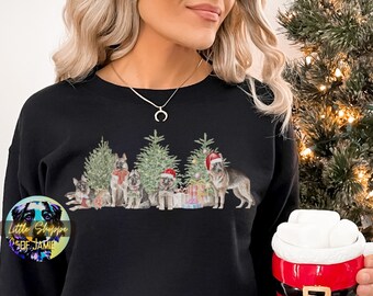 Op de afbeelding: Zwart sweatshirt met een kerstthema ontwerp met vijf Duitse herders die voor drie gedecoreerde kerstbomen staan. De honden dragen kerstmanmutsen en houden cadeaus vast.