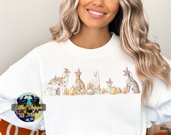 Puede incluir: Sudadera blanca con un gráfico de perros con sombreros de bruja y sosteniendo calabazas. Los perros son de diferentes razas y tamaños. El gráfico está en estilo acuarela.