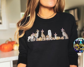 Puede incluir: Sudadera negra con un gráfico de una línea de perros con sombreros de bruja y sosteniendo calabazas. El texto "Little Shoppe of Jamie" está en un círculo en la esquina inferior derecha de la imagen.
