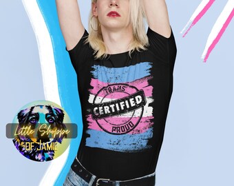 Könnte beinhalten: Ein schwarzes T-Shirt mit einem Design aus einer blauen, rosa und weißen Transgender-Pride-Flagge. Das Design enthält einen Stempel mit der Aufschrift "Trans Certified Proud".