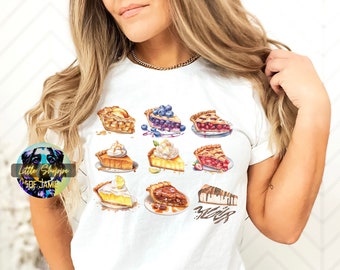 May include: A white t-shirt with a colorful illustration of different types of pie slices. The pie slices include blueberry, cherry, lemon meringue, pecan, and strawberry.
