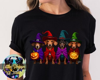 May include: A black t-shirt with a graphic of four dachshund dogs wearing witch hats and capes. The dogs are holding jack-o'-lanterns.
