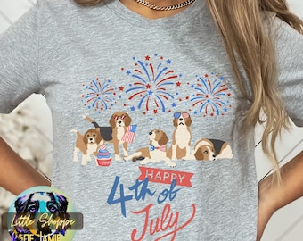 Op de afbeelding: Een grijs T-shirt met een afbeelding van vijf beagles die een zonnebril dragen en de 4e juli vieren met vuurwerk en een cupcake. De tekst "Happy 4th of July" staat op het shirt gedrukt.