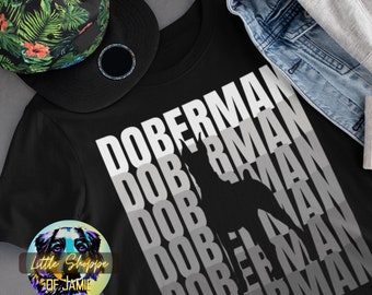 Op de afbeelding: Zwart T-shirt met een witte afbeelding van een Dobermann-silhouet en het woord "Doberman" dat in een verlooppatroon wordt herhaald.