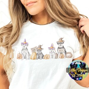 Puede incluir: Camiseta blanca con un gráfico de cinco perros vestidos con disfraces de Halloween. Los perros llevan sombreros de bruja, sostienen calabazas y uno tiene un cartel que dice "Trick or Treat".