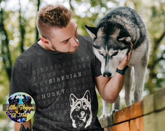 Può includere: Un uomo indossa una maglietta grigia scura con un motivo di ricerca di parole bianco che presenta la parola "Siberian Husky" ripetuta in tutto il design. L'uomo sta accarezzando un cane Siberian Husky grigio e bianco.
