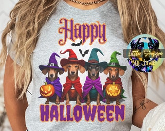 May include: A gray t-shirt with the text "Happy Halloween" in purple and orange. Four dachshund dogs wearing witch hats and capes are holding pumpkins. The text "Little Shoppe of Jamie" is in a circle in the upper right corner.