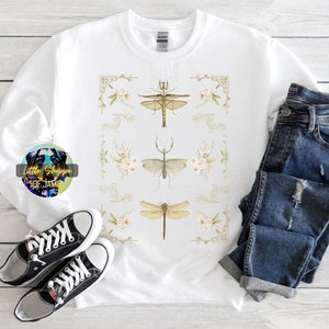 Puede incluir: Sudadera blanca con un diseño gráfico de tres mantis religiosas verdes y tres libélulas con detalles florales. El diseño está enmarcado con bordes dorados ornamentados.