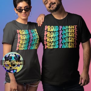 Pode incluir: Duas pessoas vestindo camisetas pretas com o texto "Proud Parent" repetido em cores do arco-íris. O texto está em um estilo de fonte retrô.