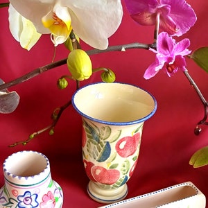 May include: A still life featuring three ceramic vases with floral designs and a branch of orchids. The vases are cream-coloured with hand-painted patterns in red, blue, and green. The orchids have white and pink blooms.
