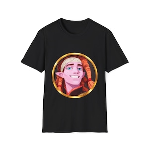 May include: Black t-shirt with a cartoon illustration of a smiling character with red braids and a white headband, framed in gold. The character has blue eyes and a pink complexion. The t-shirt is made of a soft, dark fabric.