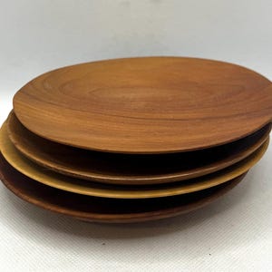 May include: A stack of four wooden plates. The plates are oval-shaped with a natural wood grain finish. The top plate is a medium brown color, with the other plates varying in shades of brown and tan.