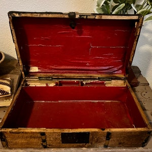 May include: An antique wooden box with a red velvet lining and a brass latch. The box has a compartment with multiple sections.