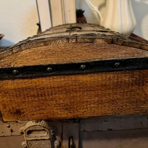 May include: A wooden box with a dark brown stain and a black leather trim with metal studs. The box has a rounded top and is closed.