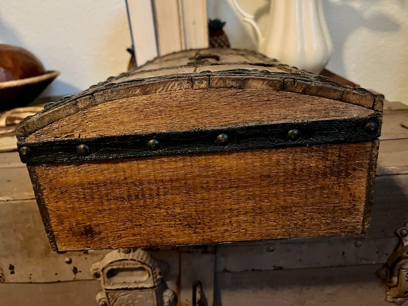 May include: A wooden box with a dark brown stain and a black leather trim with metal studs. The box has a rounded top and is closed.
