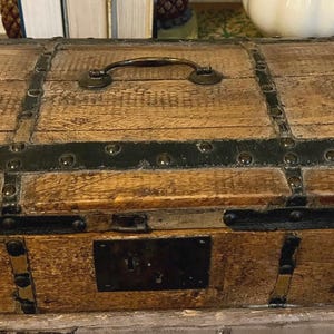 May include: A wooden chest with a hinged lid, black metal accents, and a brass handle. The chest has a dark wood finish and is decorated with metal studs.